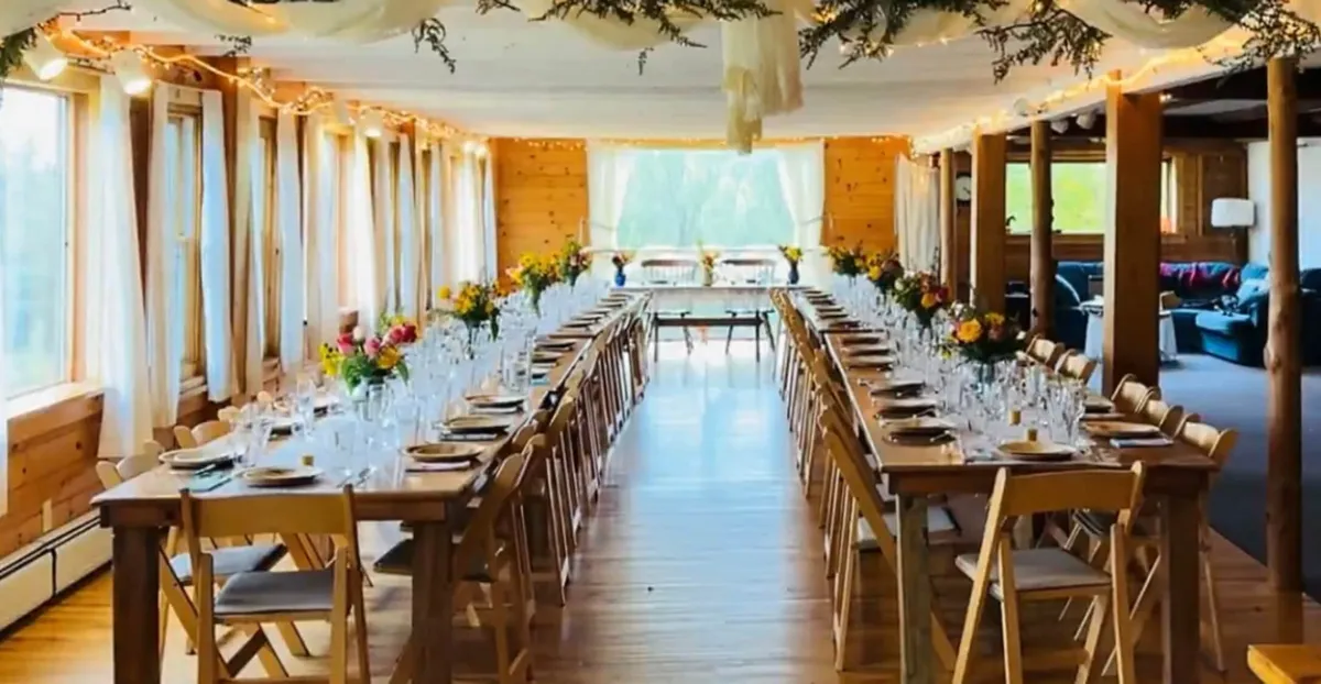 A grand communal dining area adorned with long wooden tables, floral arrangements, abundant natural wood accents, and soft drapery. Large windows flood the room with daylight, creating an uplifting ambiance that's ideal for banquets, celebrations, and heartfelt gatherings.