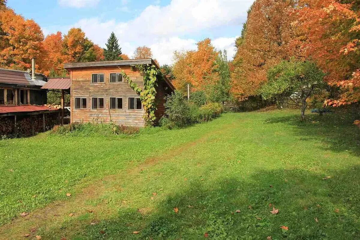 A wooden building stands among colorful autumn trees and open grassy areas, suggesting ample outdoor space for gatherings, movement classes, or group workshops. The mix of building and nature highlights the connection between indoor and outdoor wellness activities.