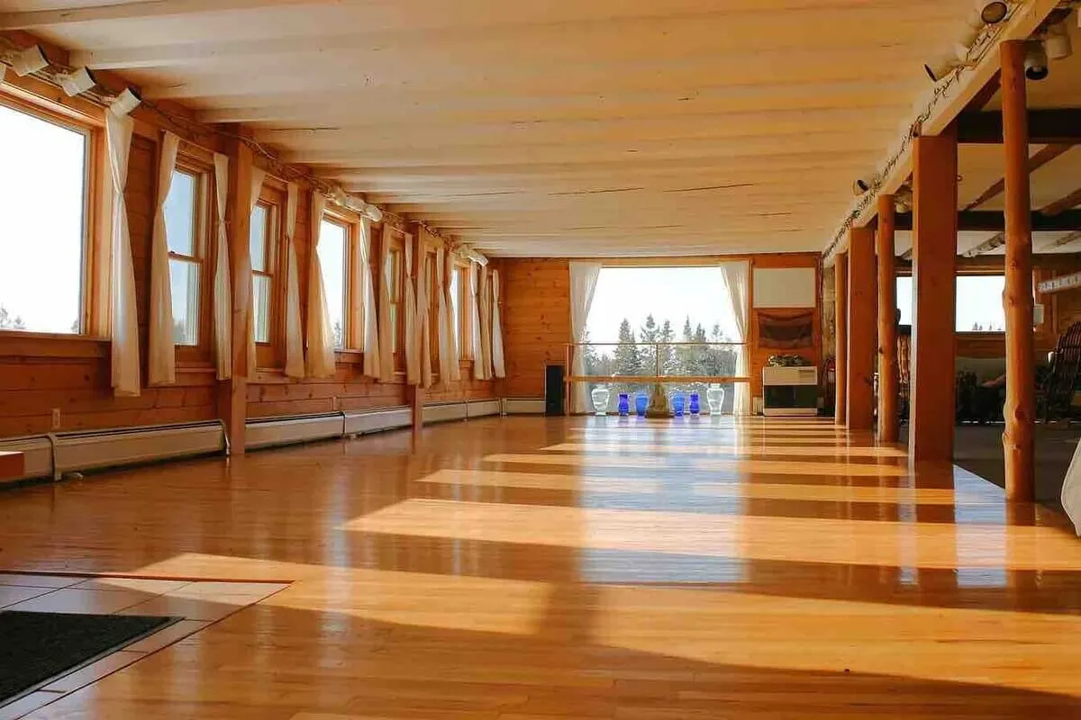 An airy, pillar-framed interior space with wooden floors and expansive windows that reveal stunning views. The open design is perfect for group events, yoga classes, workshops, or wedding receptions—the heart of community activities.