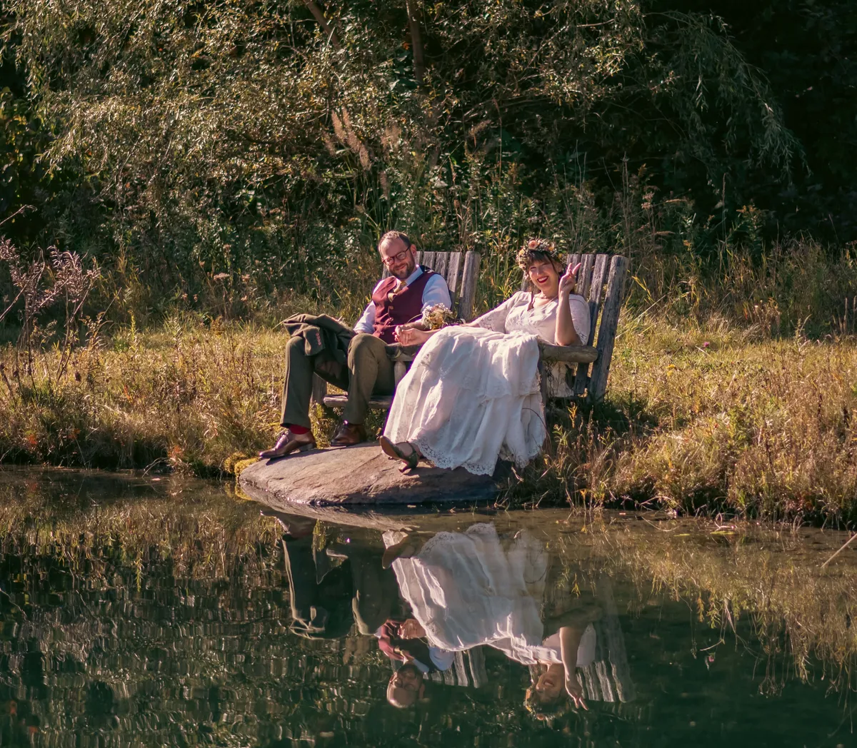 A serene pond edged by lush greenery reflects a couple sitting side-by-side, enjoying an intimate moment in nature. The tranquil water and surrounding vegetation evoke a sense of calm and offer a glimpse of private outdoor relaxation, perfect for post-hike unwinding or wildlife watching.